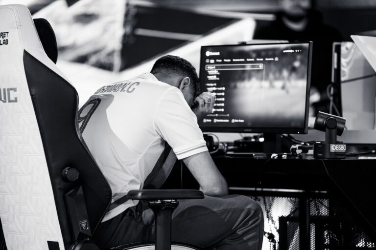 An EA FC Pro World Championship player sits frustrated in front of his console, while the tournament environment at the Esports World Cup is visible in the background.