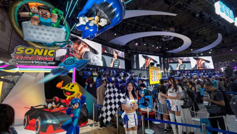 A busy Tokyo Game Show hall with large advertising displays and attendees.