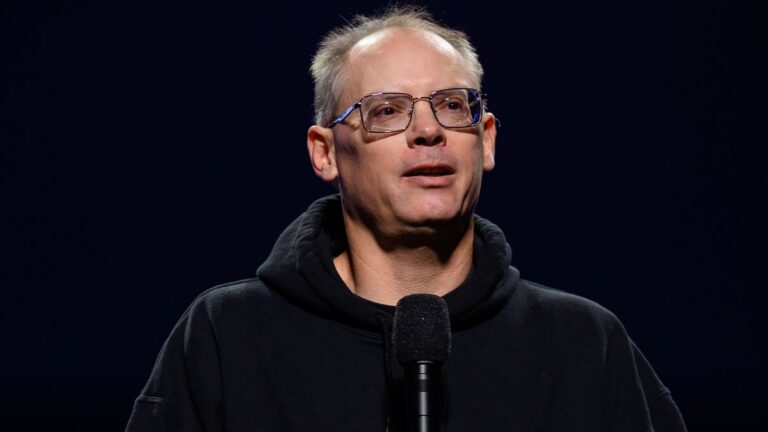 Epic-Games-Chef Tim Sweeney mit Brille und schwarzem Hoodie hinter einem Mikrofon